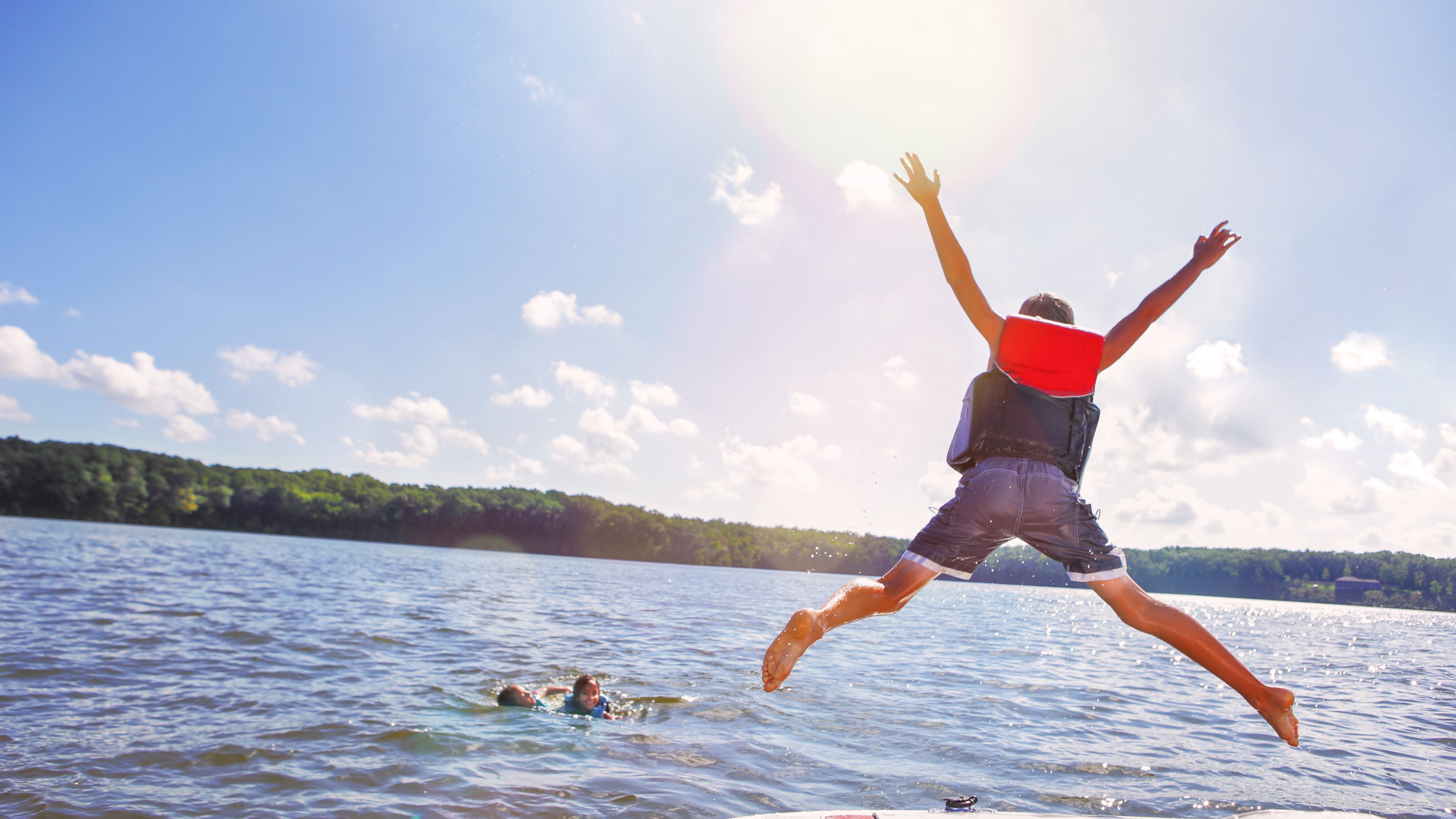 Kids jumping off a boat into the lake. Focus on boys legs and boat, some motion blur.