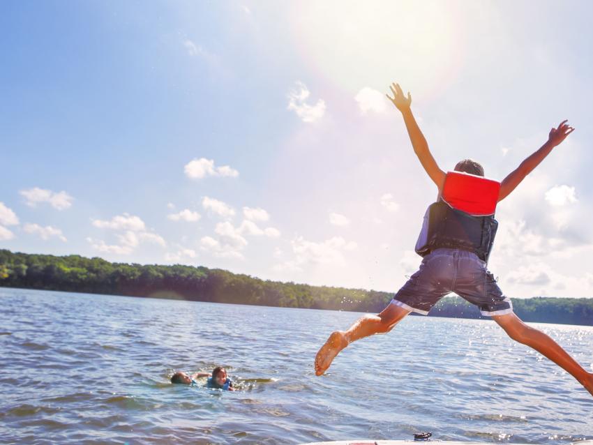 Kids jumping off a boat into the lake. Focus on boys legs and boat, some motion blur.