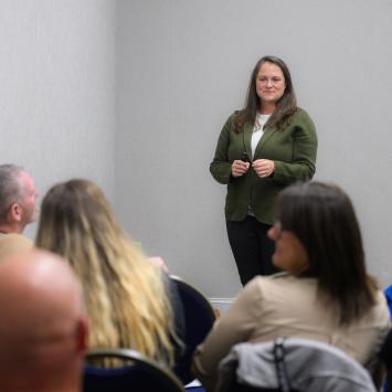 Woman stands wearing a green coat in front of an audience 